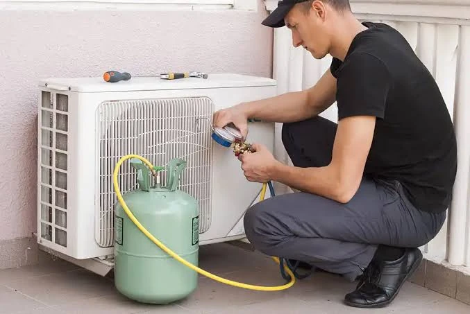 Technician using a service gauge beside a compact outdoor air conditioner