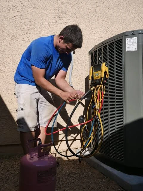 Technician inspecting refrigerant service connections on an outdoor HVAC unit